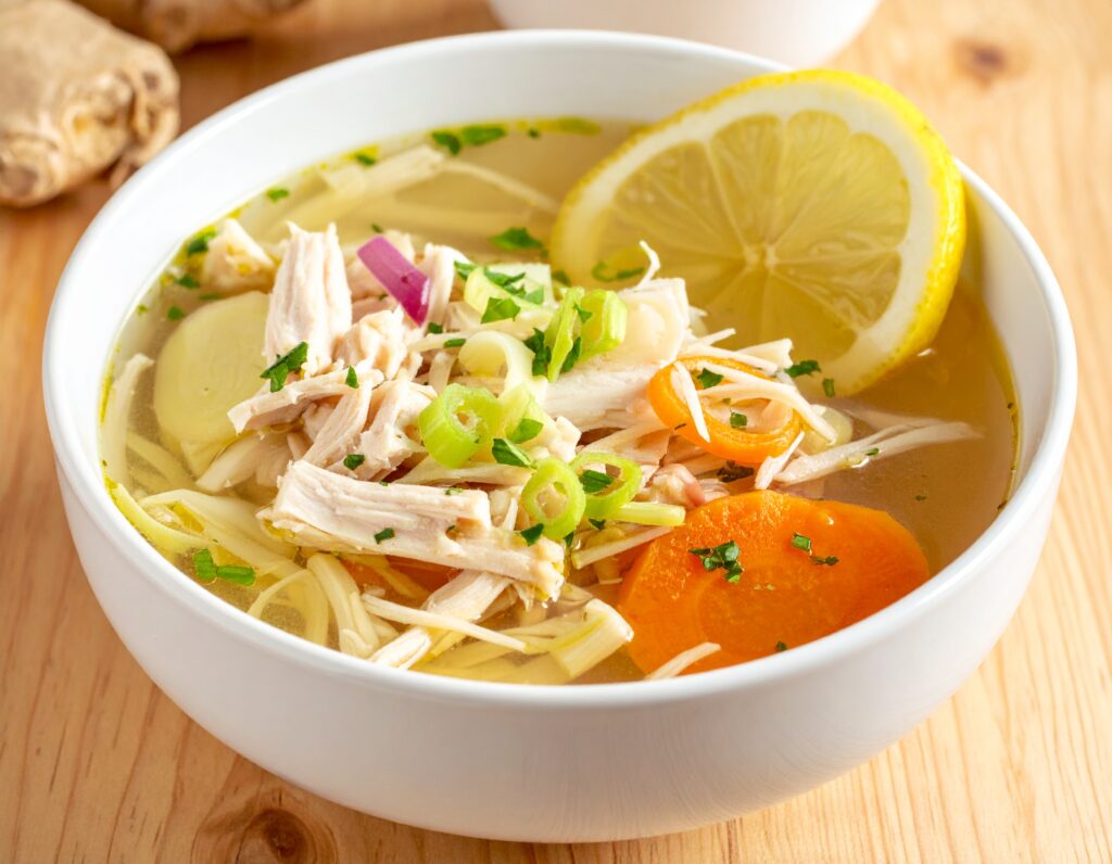 Immune-boosting ginger chicken soup with vegetables and herbs in a white bowl.