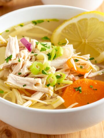 Immune-boosting ginger chicken soup with vegetables and herbs in a white bowl.