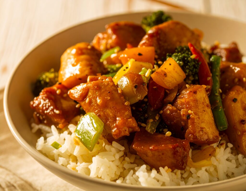 Honey garlic chicken stir fry with vegetables and rice in a white bowl.