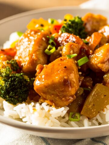Honey garlic chicken stir fry with vegetables and rice in a white bowl.