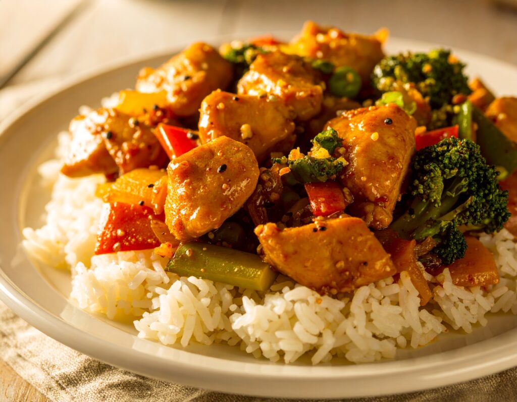 Honey garlic chicken stir fry with vegetables and rice in a white bowl.