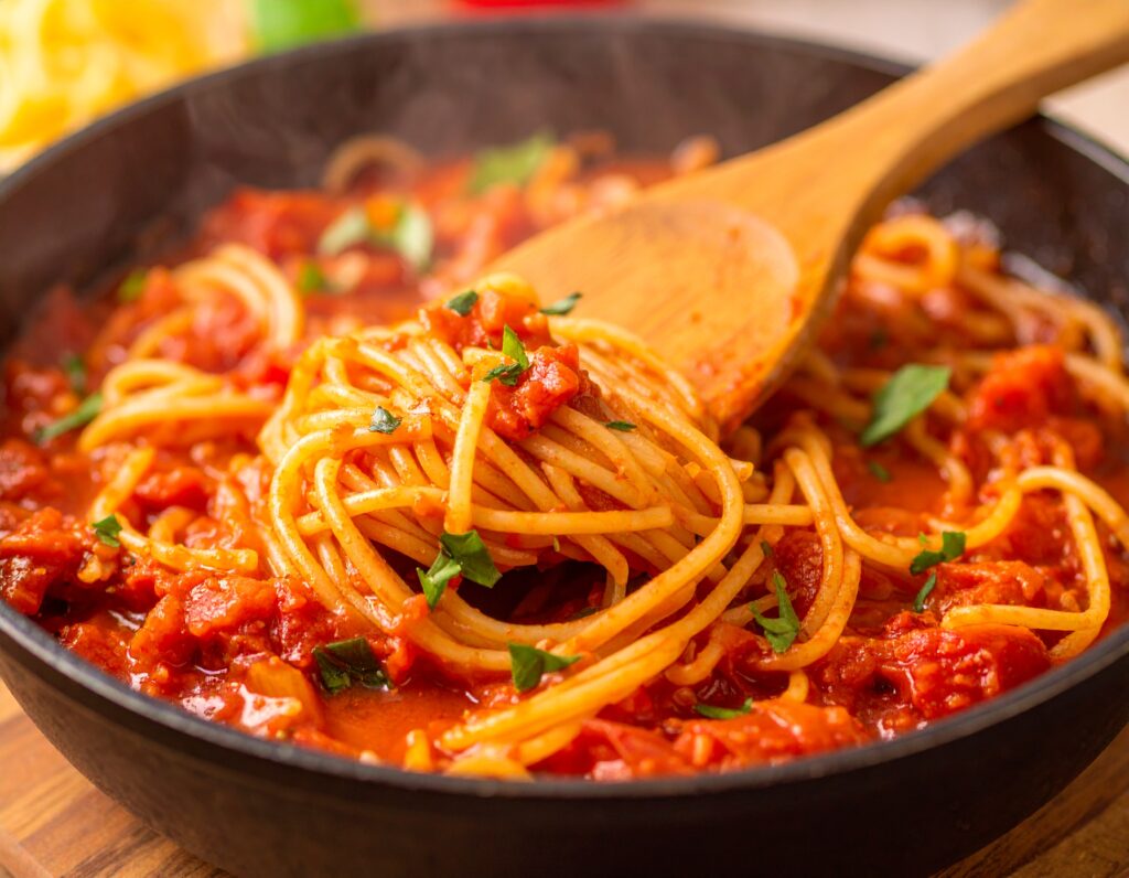 Slow-cooked crockpot spaghetti sauce in a ceramic pot with herbs and tomatoes.