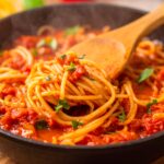 Slow-cooked crockpot spaghetti sauce in a ceramic pot with herbs and tomatoes.