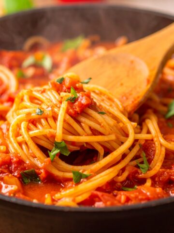 Slow-cooked crockpot spaghetti sauce in a ceramic pot with herbs and tomatoes.